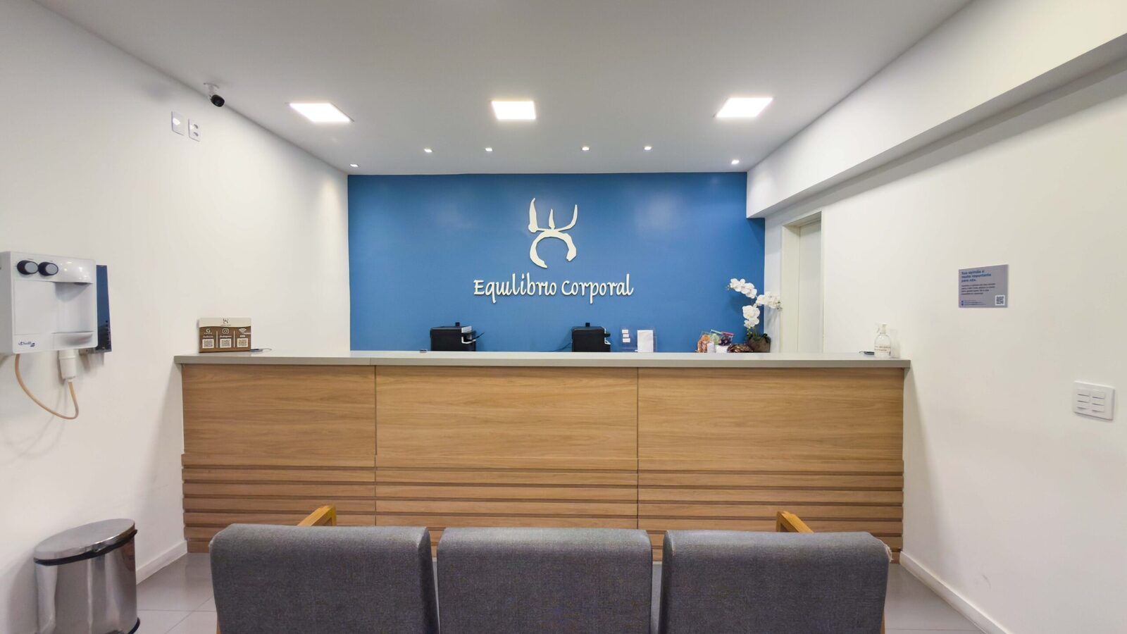Recepção da Clínica Equilíbrio Corporal, com a marca na parede azul e ambiente acolhedor